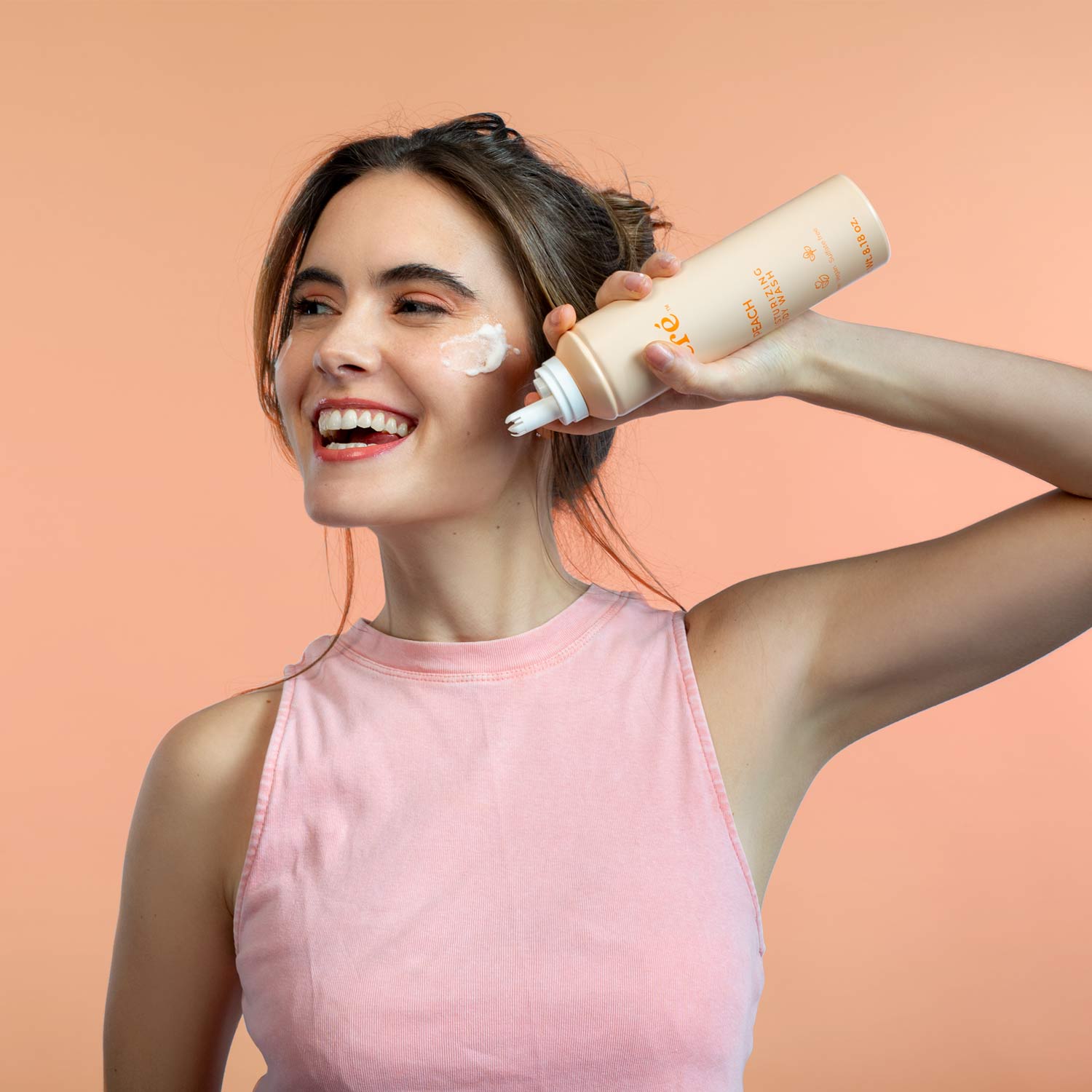 Image of a smiling girl holding the peach-scented Mecré moisturizing body wash bottle, with a foam trail on her cheek.
