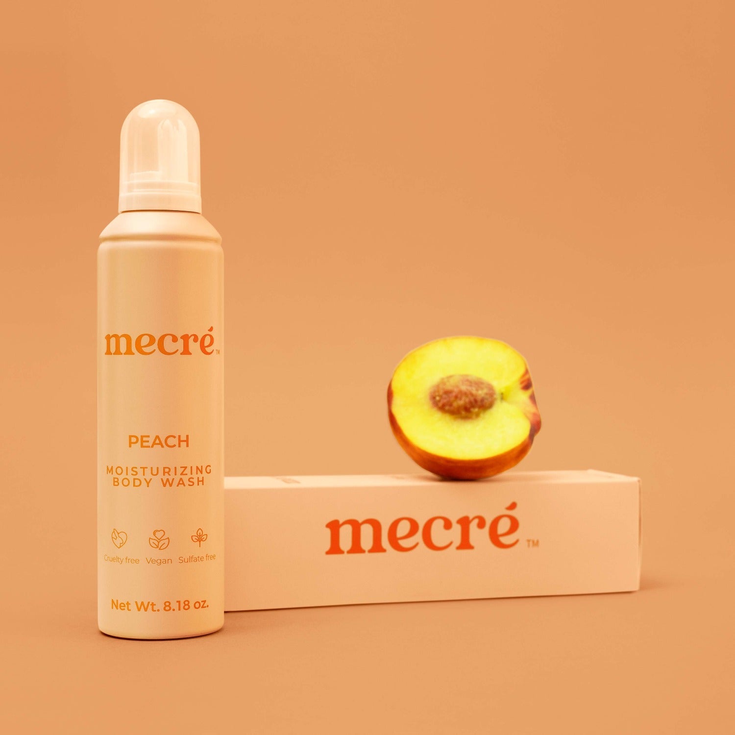 Front view of Mecré moisturizing body wash in peach scent, displayed with its packaging and half peach.